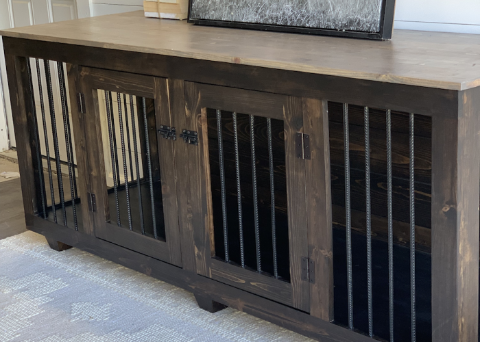 A wooden dog kennel furniture tv stand with a dark finish graces the home, featuring metal wire front doors and a framed black-and-white photograph of a dog on top, nestled among books and a small potted plant.